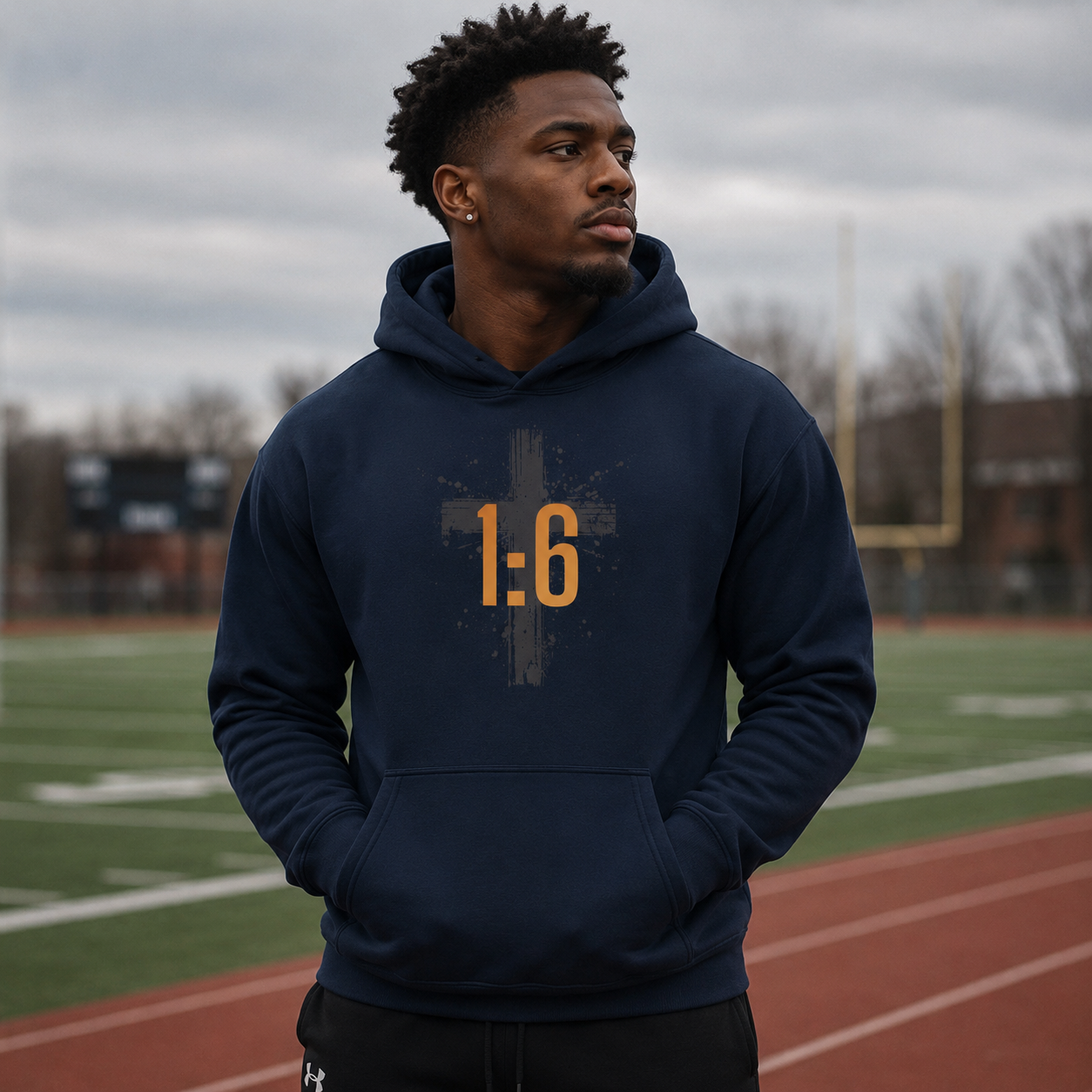 Man wearing a navy hoodie with '1:6' printed on it, standing on a track field.